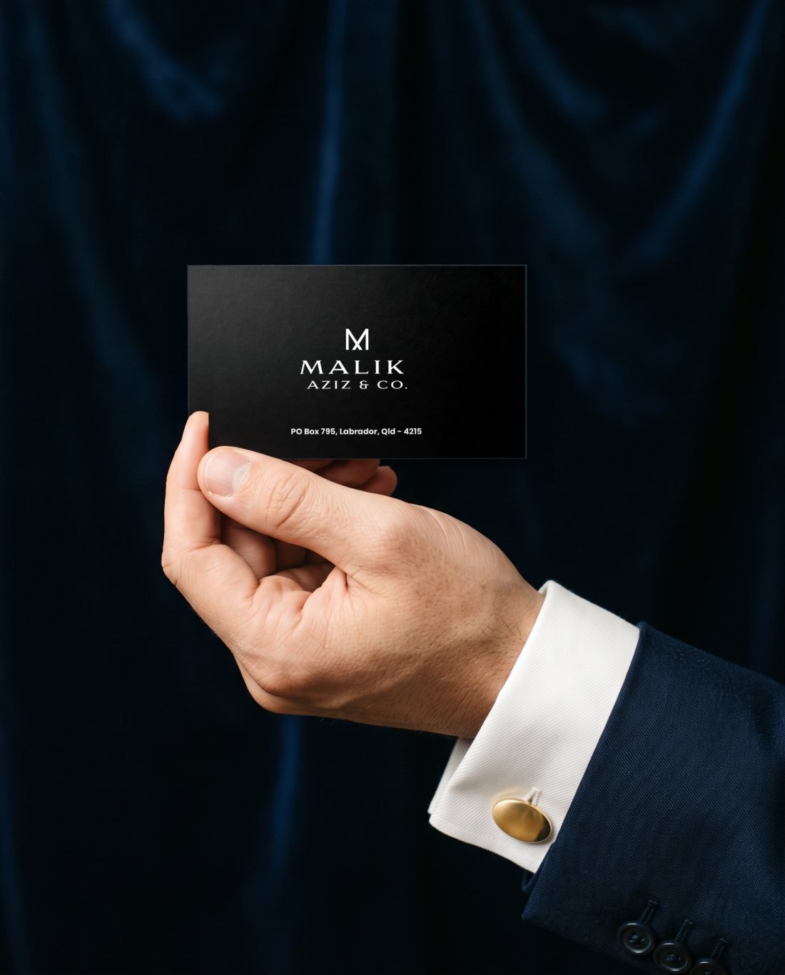 A hand in a navy suit cuff presenting a Malik Aziz and Co. business card
